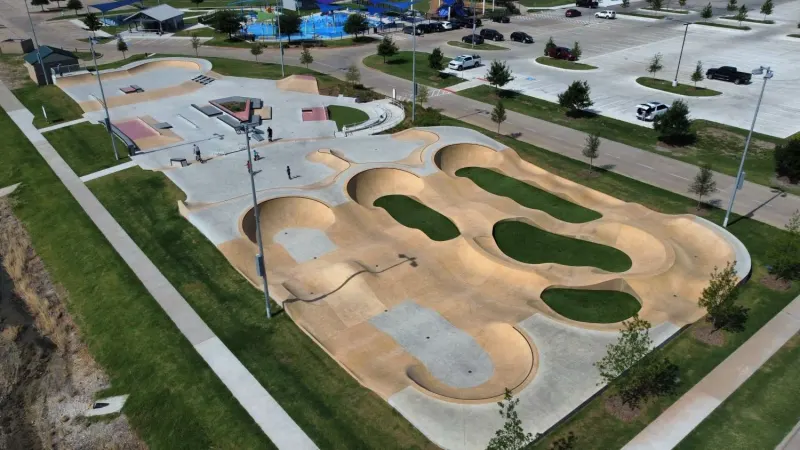 Aerial view of Slayter Creek Skatepark in Anna, Texas: a large concrete park with two bowls and street features, surrounded by grass