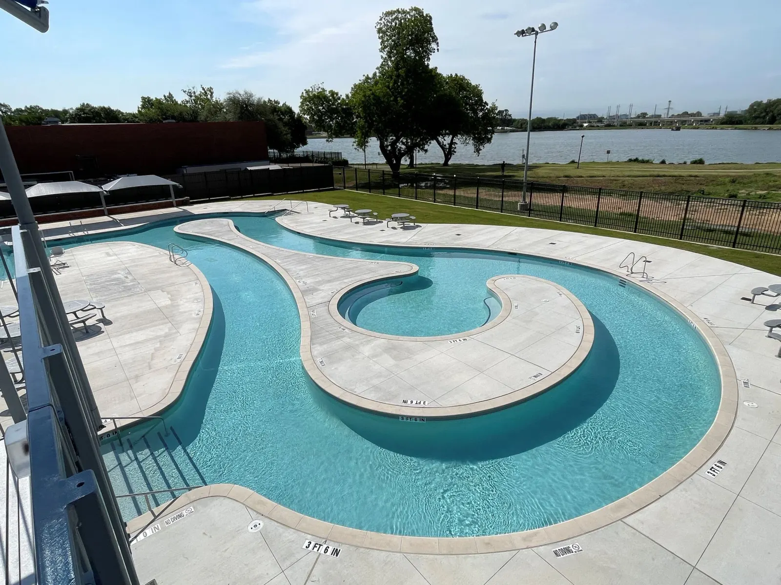 The curved outdoor pool at the Bachman Aquatic Center, with trees and a light pole behind it