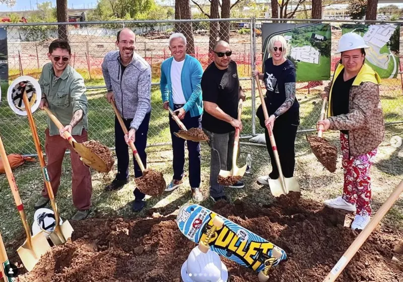 City officials and skaters in hard hats turning earth with ceremonial shovels at the Bachman Lake Skatepark groundbreaking